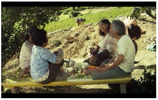 Just before the transition into slasher violence, the village elders enjoy food and drink while Pong-nam toils in the fields.